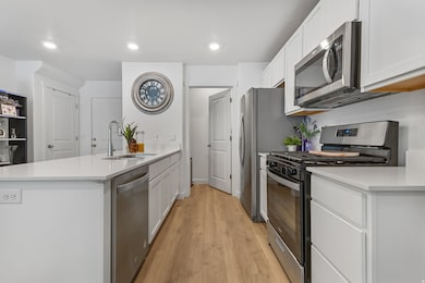 Kitchen featuring stainless steel appliances, a peninsula, recessed lighting, light wood-style floors, and sleek white cabinetry