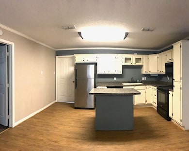 Kitchen with a kitchen island, black appliances, dark wood finished floors, crown molding, and dark countertops