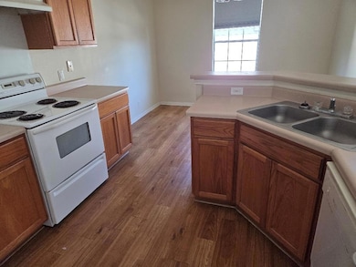 Kitchen with white appliances, dark wood-style flooring, light countertops, and brown cabinets