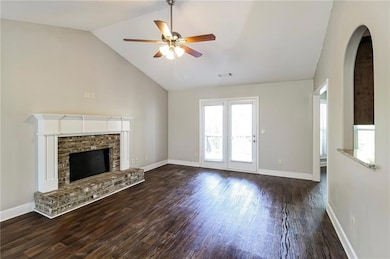 Unfurnished living room with dark wood finished floors, ceiling fan, a fireplace, arched walkways, and high vaulted ceiling