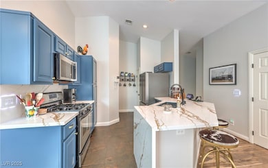 Kitchen with blue cabinets, stainless steel appliances, light stone counters, a kitchen breakfast bar, and backsplash