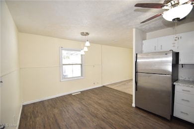 Kitchen featuring freestanding refrigerator, hanging light fixtures, a textured ceiling, dark wood-type flooring, and white cabinetry