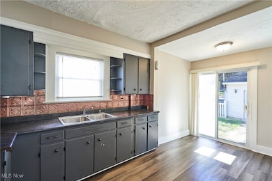 Kitchen featuring dark countertops, open shelves showcasing decor, a decorative backsplash, updated gray cabinets, and new LVT flooring. A sliding glass door provides access to a conveniently fenced backyard.