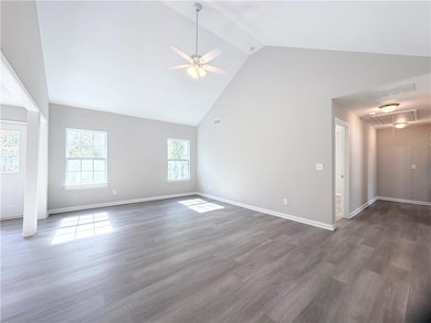 Unfurnished living room featuring attic access, high vaulted ceiling, dark wood finished floors, and ceiling fan