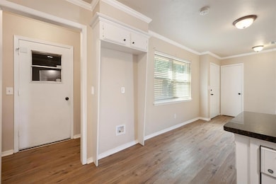 Kitchen featuring white cabinetry, ornamental molding, light wood-style floors, and dark stone countertops