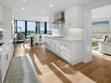 Kitchen featuring white cabinets, recessed lighting, light wood finished floors, wall chimney range hood, and light stone countertops