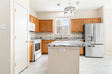 Kitchen with white appliances, a center island, light stone countertops, hanging light fixtures, and brown cabinetry