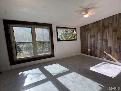 Unfurnished room featuring wood walls, a textured ceiling, and a ceiling fan