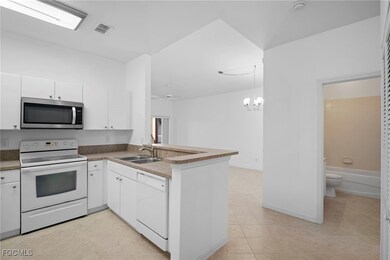 Kitchen with white appliances, a peninsula, white cabinets, and light tile patterned floors