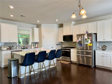 Kitchen featuring stainless steel appliances, decorative backsplash, white cabinets, light countertops, and kitchen island with breakfast bar