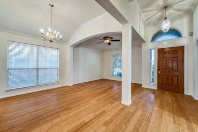 Entryway with ornamental molding, a chandelier, light wood finished floors, high vaulted ceiling, and a ceiling fan