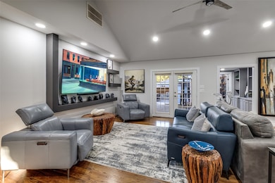 Beautifully lit living room with vaulted ceiling, custom wall shelving, and double doors to the backyard. Includes view of the hallway leading to the home’s flex space.