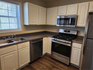 Kitchen featuring appliances with stainless steel finishes, dark countertops, a sink, white cabinets, and dark wood-style floors