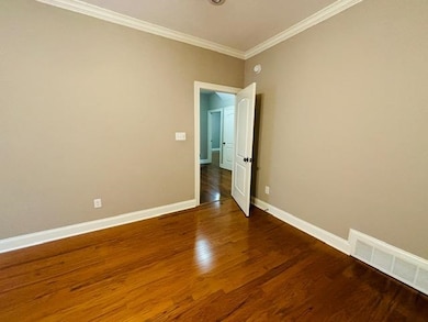 Spare room featuring crown molding, wood finished floors, and baseboards