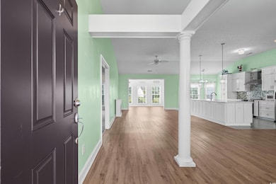 Foyer entrance with a ceiling fan, light wood-style floors, baseboards, and decorative columns