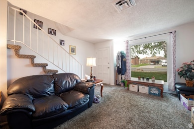 Living room with stairway, visible vents, a textured ceiling, and carpet floors