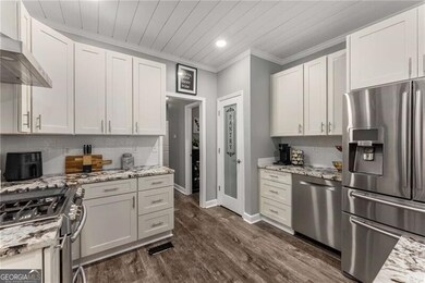 Kitchen featuring appliances with stainless steel finishes, ventilation hood, dark wood finished floors, backsplash, and crown molding