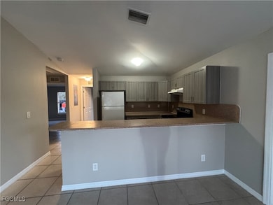Kitchen with freestanding refrigerator, black / electric stove, dark countertops, a peninsula, and light tile patterned floors