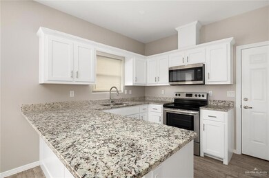 Kitchen with stainless steel appliances, a peninsula, white cabinetry, and light wood finished floors