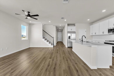 Kitchen with white cabinets, backsplash, stainless steel appliances, light wood-style flooring, and a center island with sink