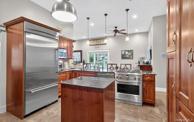 Kitchen featuring appliances with stainless steel finishes, a peninsula, a kitchen island, decorative light fixtures, and dark stone counters