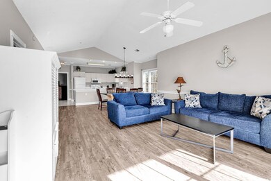 Living area featuring lofted ceiling, light wood-type flooring, baseboards, ceiling fan with notable chandelier, and visible vents