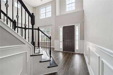 Living room with wood finished floors, a chandelier, a towering ceiling, a wainscoted wall, and a decorative wall