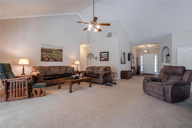 Living area with carpet flooring, high vaulted ceiling, and a ceiling fan