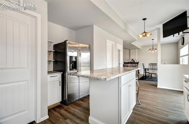 Kitchen featuring white cabinets, stainless steel refrigerator with ice dispenser, a breakfast bar, dark wood finished floors, and hanging light fixtures