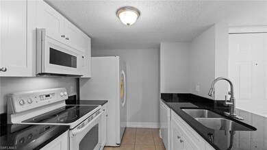 Kitchen with white appliances, a sink, white cabinetry, a textured ceiling, and dark stone countertops