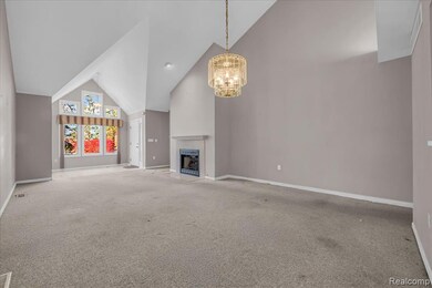 Unfurnished living room featuring high vaulted ceiling, a fireplace with flush hearth, a chandelier, and carpet floors