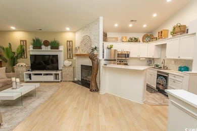 Kitchen featuring a fireplace, stainless steel appliances, open floor plan, light countertops, and a sink