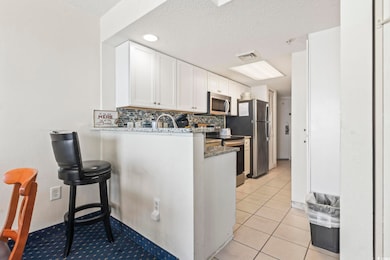 Kitchen featuring white cabinets, tasteful backsplash, dark stone countertops, appliances with stainless steel finishes, and light tile patterned flooring