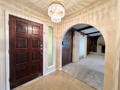 Carpeted foyer featuring beamed ceiling, arched walkways, a chandelier, and tile patterned floors