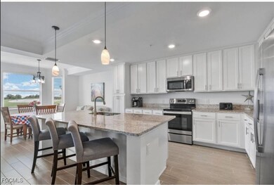 Kitchen featuring stainless steel appliances, decorative light fixtures, white cabinets, a breakfast bar, and light stone countertops