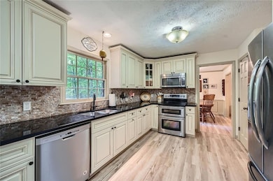 Kitchen featuring appliances with stainless steel finishes, a sink, cream cabinetry, updated floors, and tasteful backsplash