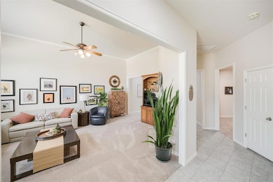 Living room featuring ceiling fan, baseboards, light carpet, ornamental molding, and light tile patterned floors