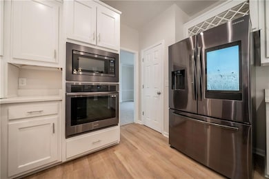 Kitchen with appliances with stainless steel finishes, light wood-style flooring, white cabinets, and light countertops