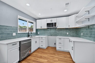 Kitchen with white cabinets, open shelves, light wood-style floors, stainless steel dishwasher, and recessed lighting