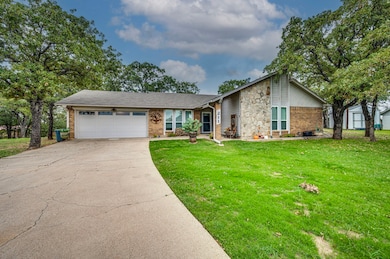 View of front facade featuring a garage, driveway, brick siding, a front lawn, and stone siding