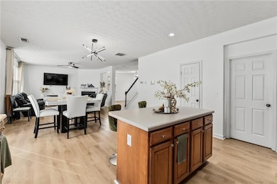 Kitchen featuring a center island, light wood-style floors, open floor plan, ceiling fan, and a textured ceiling
