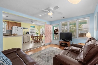 Living room with light wood finished floors, healthy amount of natural light, a textured ceiling, and a ceiling fan