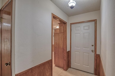 Corridor featuring a textured ceiling, wood walls, and light tile patterned flooring