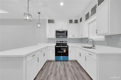 Kitchen with range with electric cooktop, stainless steel microwave, a peninsula, white cabinetry, and light countertops