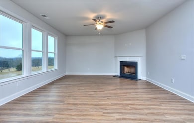 Unfurnished living room featuring light wood finished floors, a fireplace with raised hearth, and ceiling fan