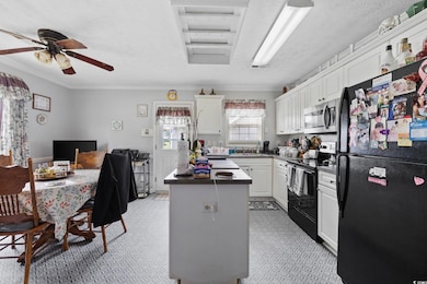 Kitchen featuring black appliances, a center island, white cabinets, crown molding, and a textured ceiling