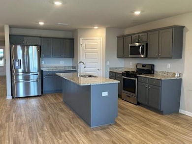 Kitchen with stainless steel appliances, light wood-style floors, light stone countertops, an island with sink, and recessed lighting