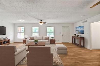 Living area with ceiling fan, a textured ceiling, light wood-style floors, and baseboards