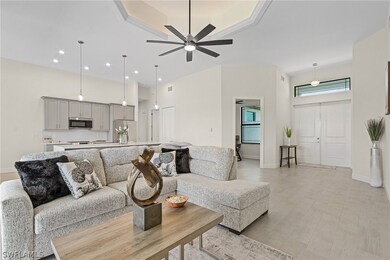 Living room with a high ceiling, light hardwood / wood-style floors, ceiling fan, and a raised ceiling