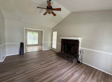 Unfurnished living room featuring lofted ceiling, a stone fireplace, wood finished floors, and a ceiling fan